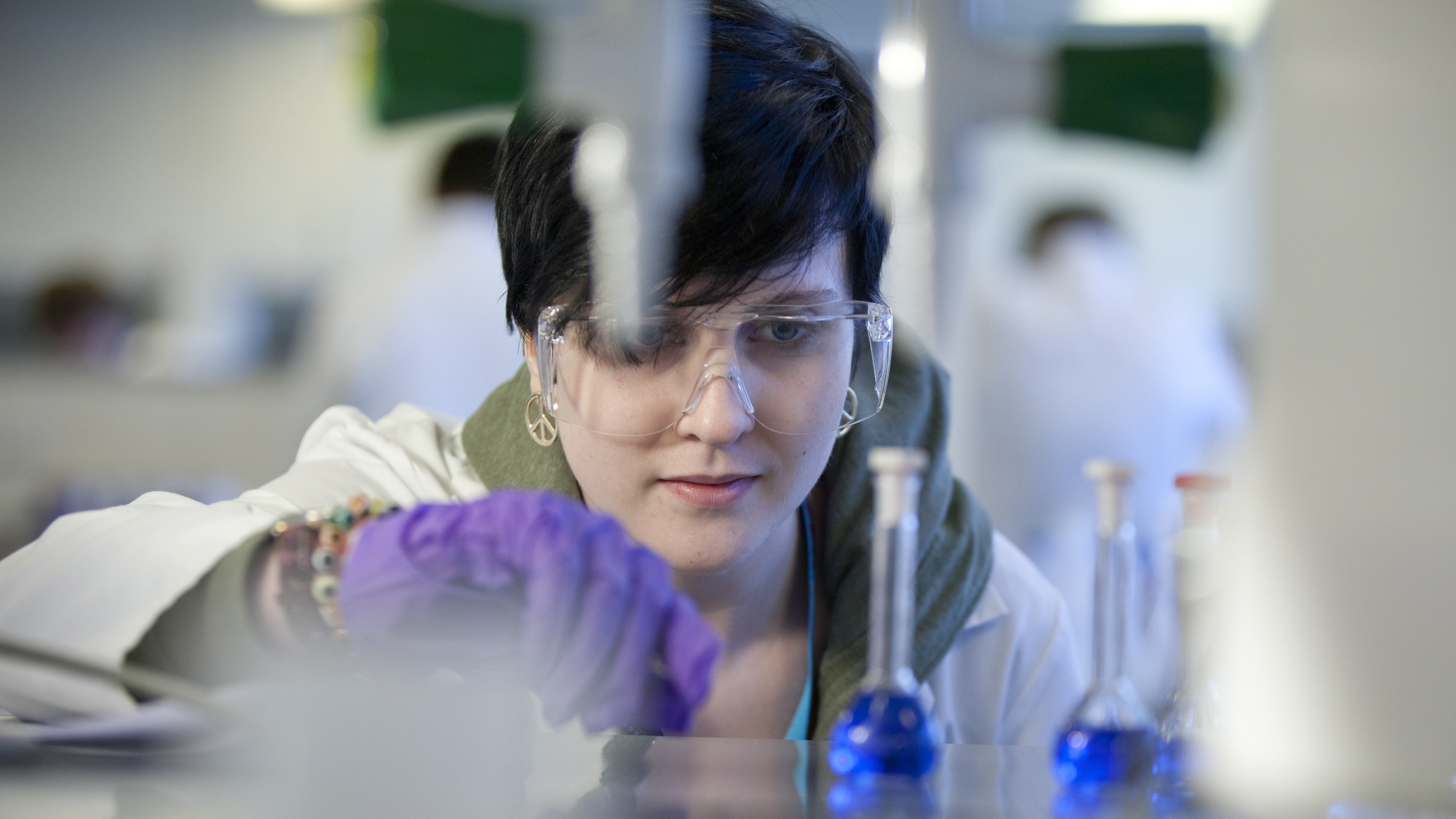 Student wearing safety goggles in a laboratory, doing a science experiment.