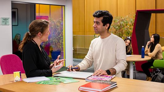 Male postgraduate student talking to a member of staff in the student hub