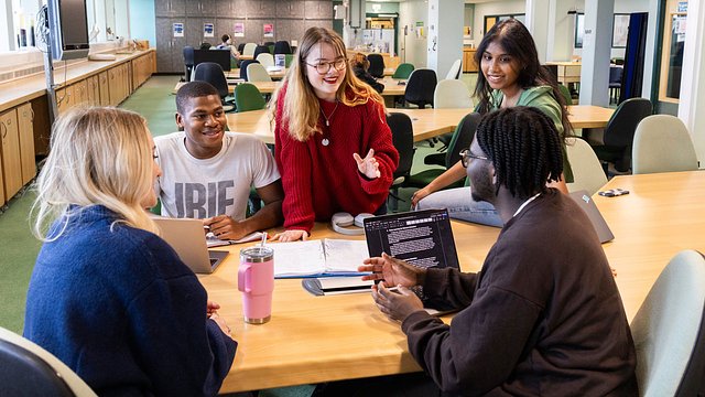 A groups of students discussing work or studying around a table in the library.