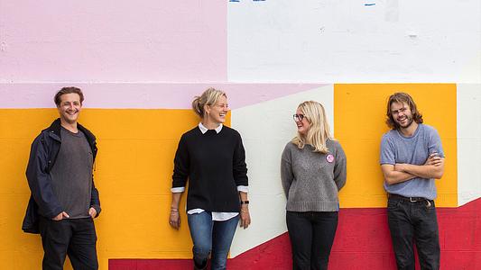 group of four students standing in front of colourful wall.