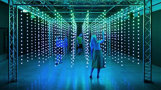 People walking through an immersive installation of hanging lights, by Squidsoup