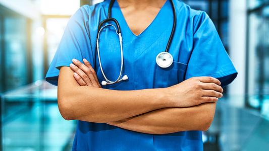 Medical staff standing with arms folded in blue scrubs with stethoscope around their neck