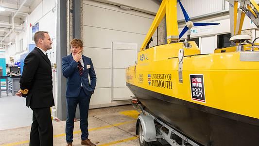 Representatives of the Royal Navy and University of Plymouth meet beside Uncrewed Surface Vessel (USV) Cetus at the launch of the National Centre for Coastal Autonomy