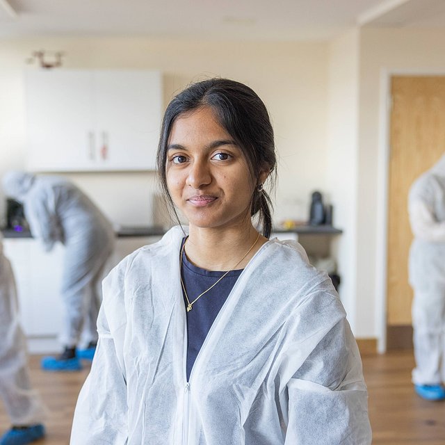 Sidney De Souza - Criminology Student poses in the murder house while students work around her