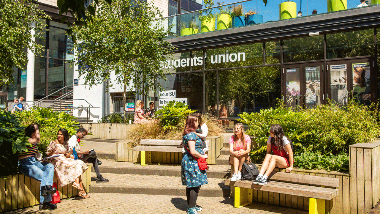 Students and Ambassadors on campus during an Open Day, sitting in the sun outside the Students' Union entrance